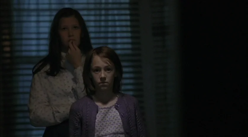 Ratcatcher (1999) movie still: medium — Two young girls stand inside a dimly lit space against a window with blinds. The scene is dark, focusing on…