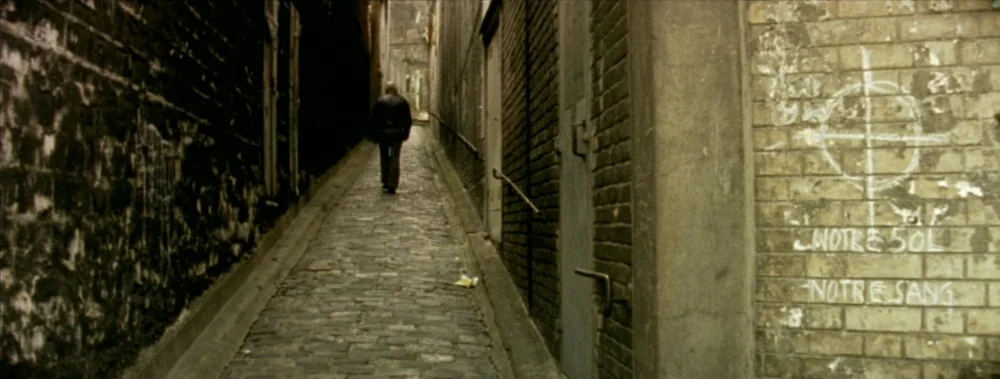 I Stand Alone (Seul Contre Tous) (1998) movie still: wide — A narrow cobblestone walkway is framed by dark, weathered brick walls on both sides. A…