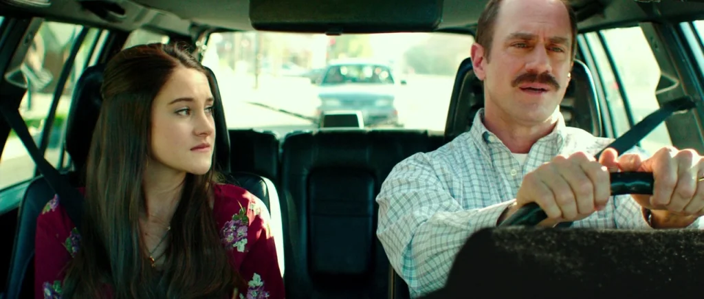 White Bird in a Blizzard (2014) movie still: medium — The interior of a car shows a man driving and a woman sitting passenger. Bright daylight…