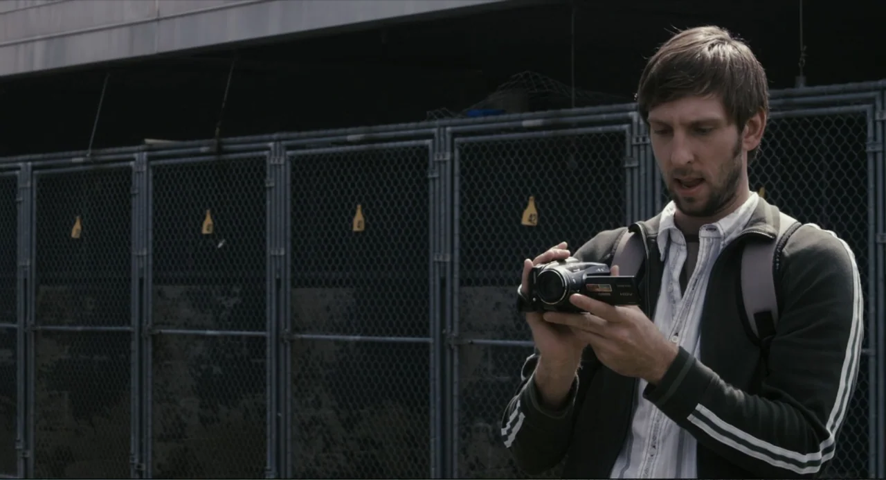 Beyond a Reasonable Doubt (2009) movie still: medium — A man stands outdoors in front of a series of metal chain-link storage lockers. He holds a…