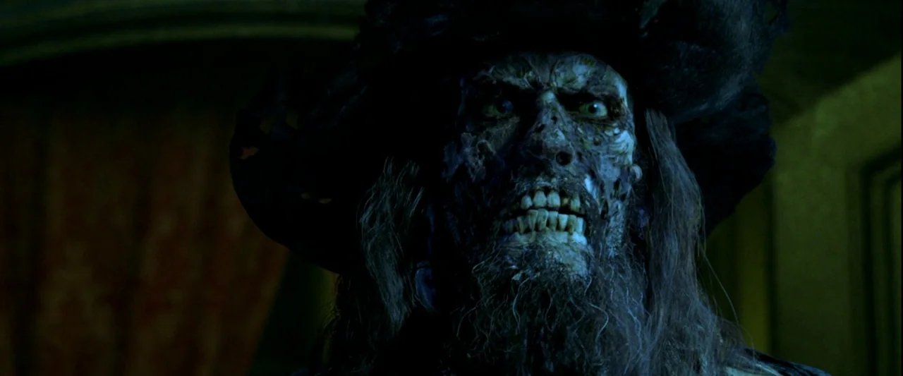 Pirates of the Caribbean: The Curse of the Black Pearl movie still: closeup — A dimly lit cabin features dark wooden walls and textured, decaying…
