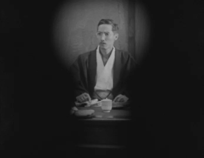 Tokyo Chorus (1931) movie still: medium — A dimly lit room is visible only through a circular keyhole-style vignette. A man in a kimono sits behind…