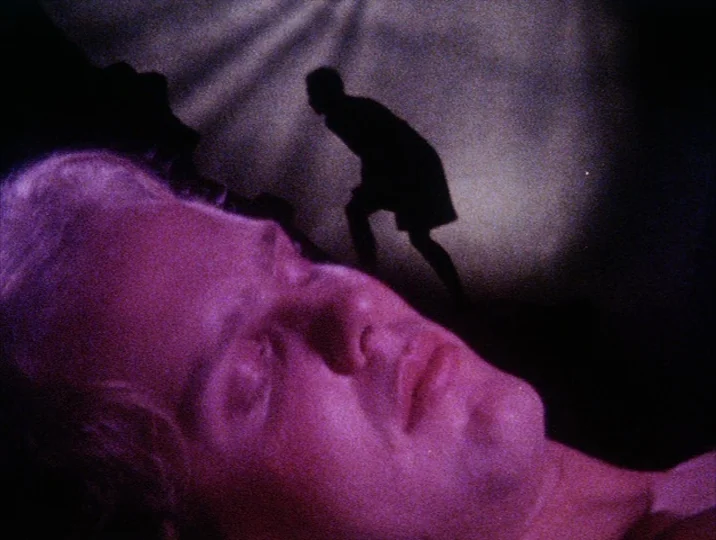 Careful (1992) movie still: closeup — A close-up shot focuses on the sleeping face of a man in a dark room. A dark, indistinct shadow figure is…