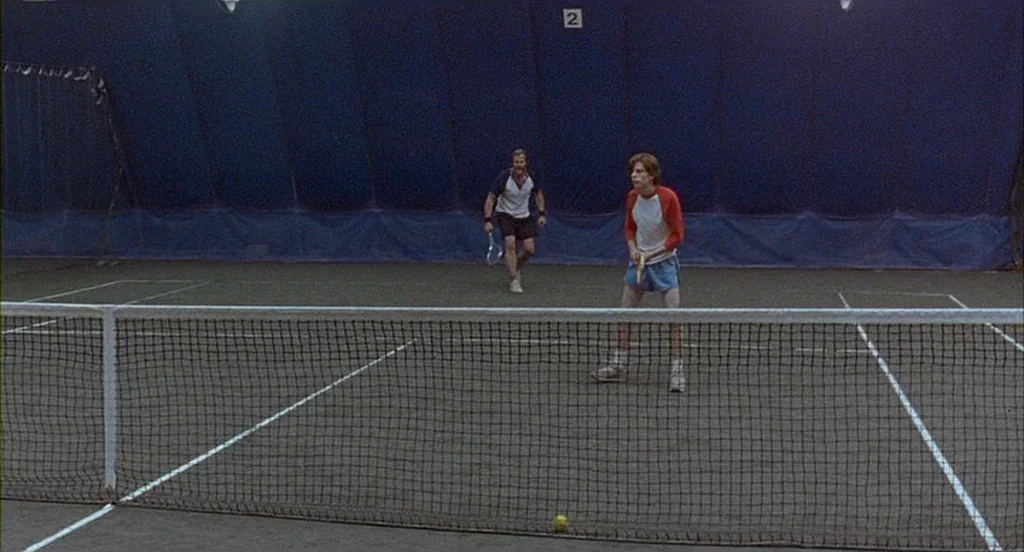 The Squid and the Whale (2005) movie still: wide — An indoor tennis facility features a dark blue curtained backdrop behind the green court surface.…