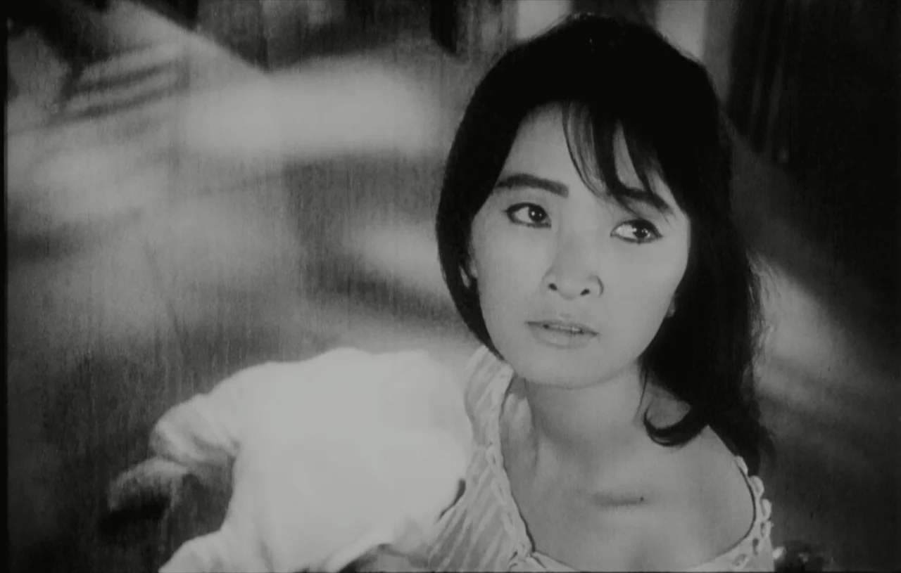 The Housemaid (1960) movie still: closeup — An interior space displays monochromatic tones with blurred background elements. A woman gazes upward…