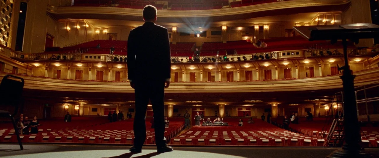 Steve Jobs (2015) movie still: fullbody — An empty auditorium features rows of red velvet seats beneath ornate gold-trimmed balconies. A man in a…