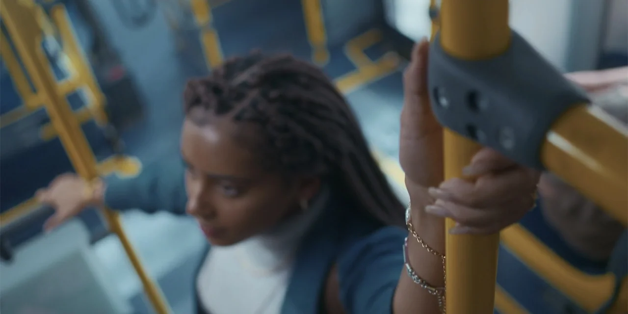 An Unforgettable Year - Autumn (2023) movie still: closeup — An interior of a public bus with yellow poles and blue seating. A woman with braided…