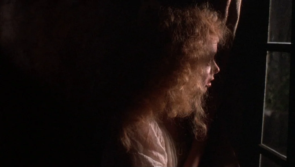 The Company of Wolves (1984) movie still: closeup — A dimly lit room at night with dark surroundings and a single window source. A young woman with…