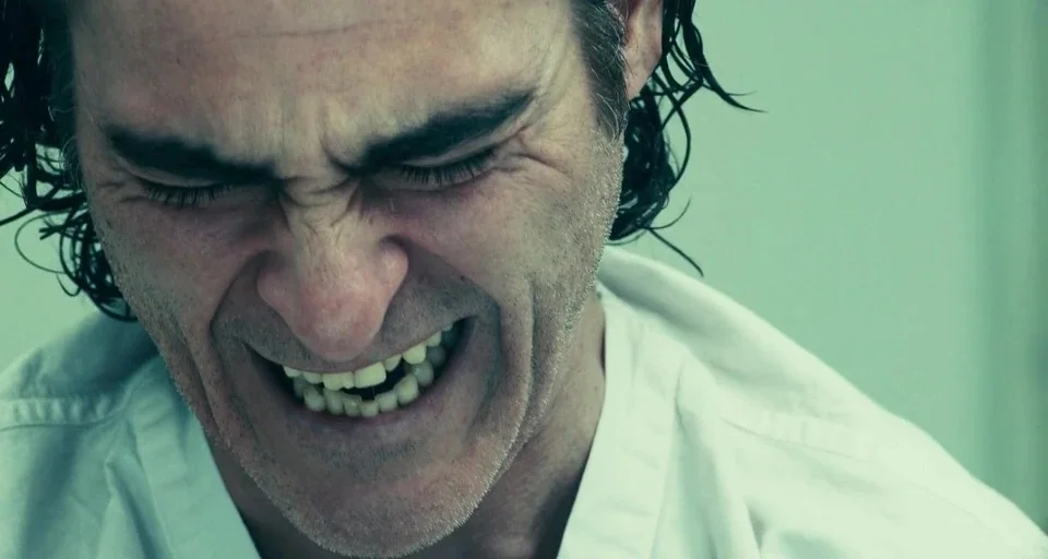 Joker (2019) movie still: closeup — A clinical interior space with a pale, sterile color scheme and high-key lighting. An adult male with dark hair…