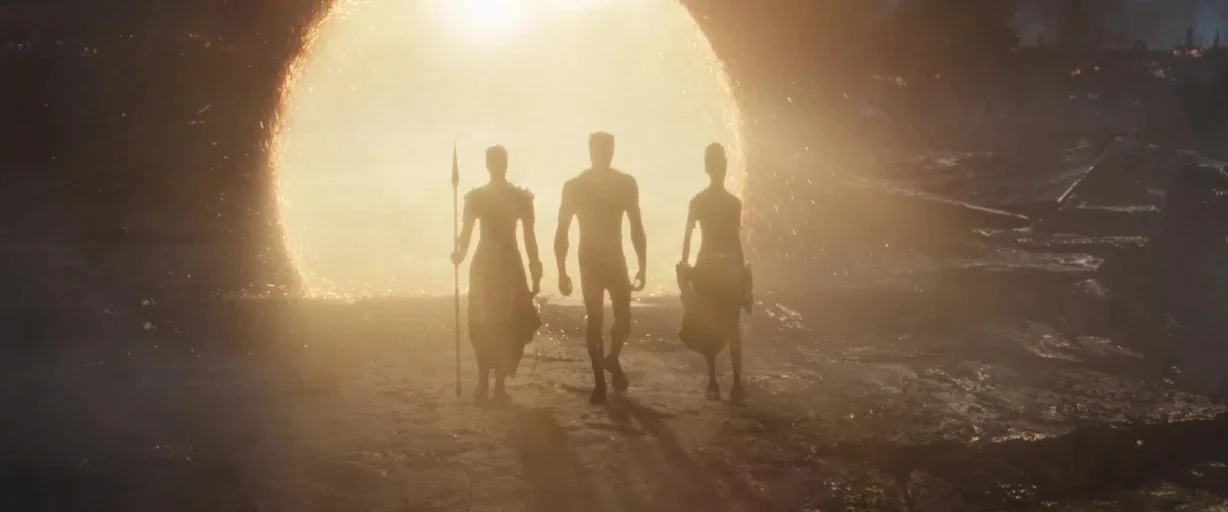 Avengers: Endgame (2019) movie still: fullbody — Three figures stand in silhouette on a dark, rugged surface before a bright portal. The trio walks…