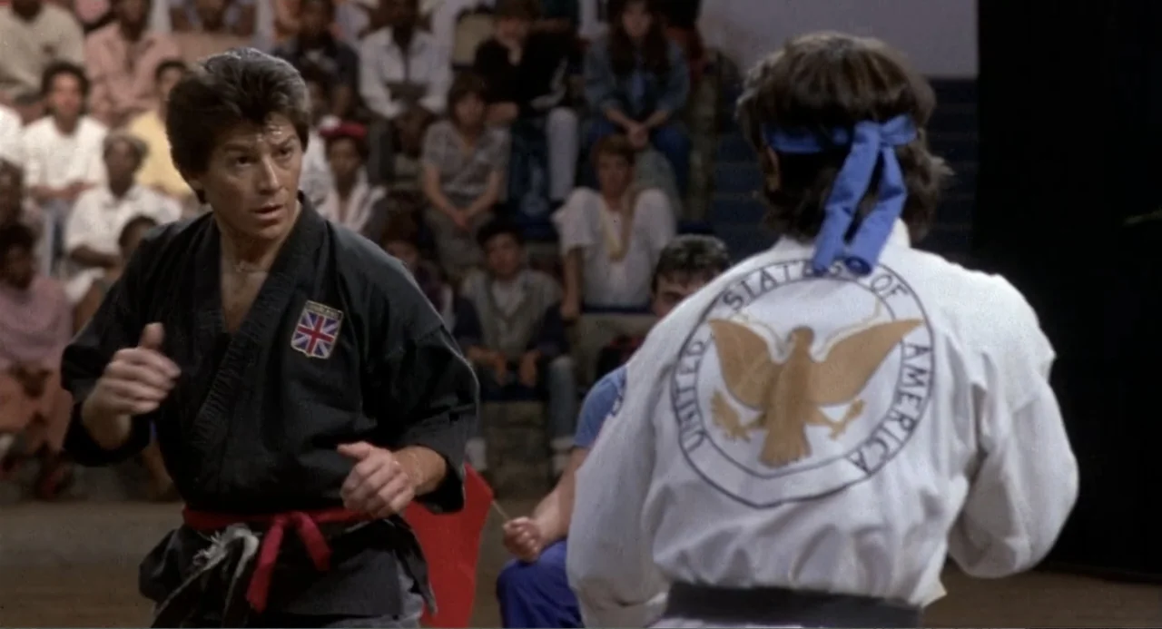 American Ninja 3: Blood Hunt (1989) movie still: medium — A gymnasium interior features bleachers filled with spectators in the background. Two men…
