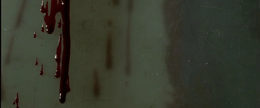 Let The Right One In (2008) movie still: closeup — A close-up view of a smooth, dark-gray surface with faint vertical striations. Dark red liquid…