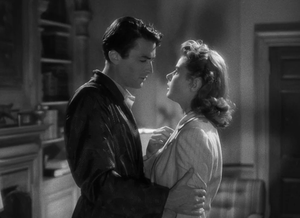 Spellbound (1945) movie still: medium — A library with built-in wooden bookshelves and a doorway in the background. A man and woman stand in close…