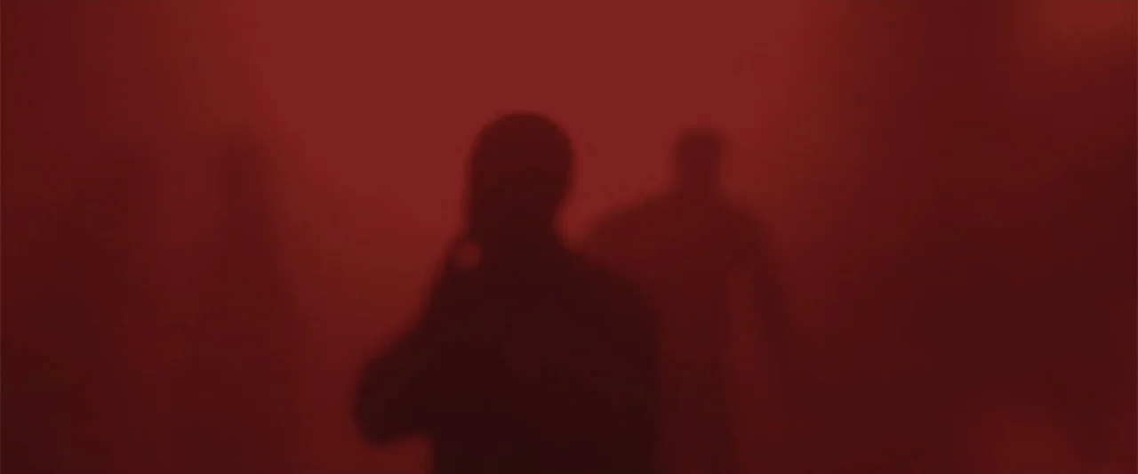 Ghosts of the Ozarks (2022) movie still: medium — A dense interior space is completely filled with thick, vibrant red smoke. Two silhouettes stand…
