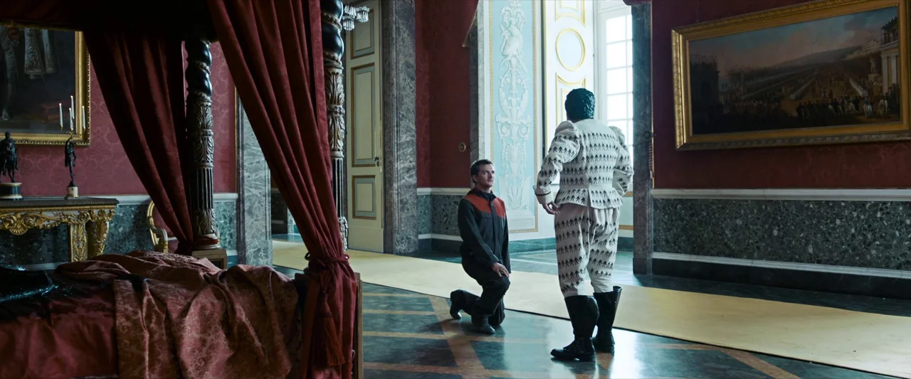 Godzilla x Kong: The New Empire (2024) movie still: wide — A spacious room features high ceilings, red walls, and a large four-poster bed. One man…