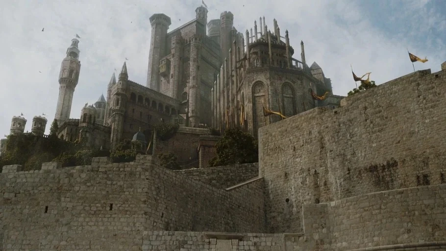 Game of Thrones (2015) movie still: establishing — A massive grey stone medieval fortress features towering spires and thick perimeter walls.…