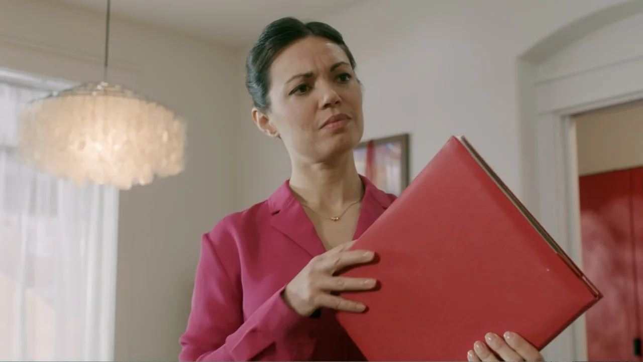 Peppermint and Postcards (2023) movie still: medium — A well-lit residential living room contains a white ceiling light fixture and a door frame. A…