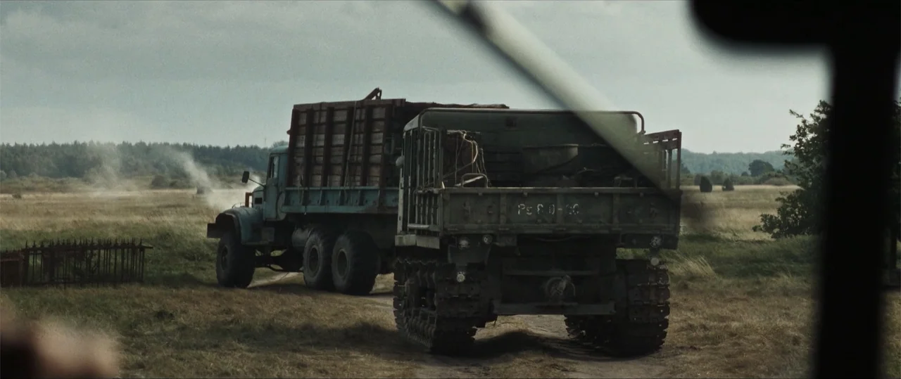 Sisu: Road to Revenge (2025) movie still: wide — A vast, grassy field stretches toward a distant tree line under a cloudy sky. A large, weathered…