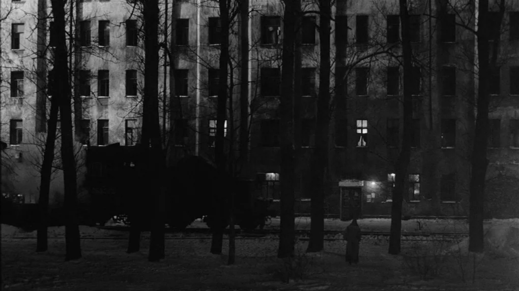 The Role (2013) movie still: wide — A snowy courtyard stands before a large, multistory tenement building at night. A lone figure in a long dark…