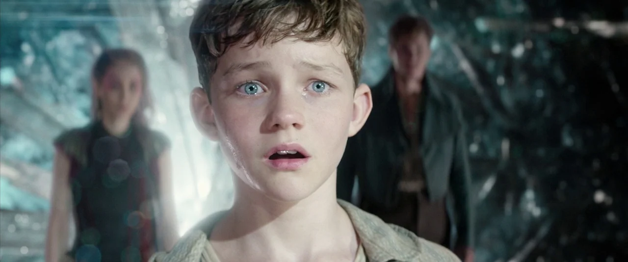 Pan (2015) movie still: closeup — A dimly lit, crystalline cavern provides a dark and textured background behind the subject. A young boy stands in…