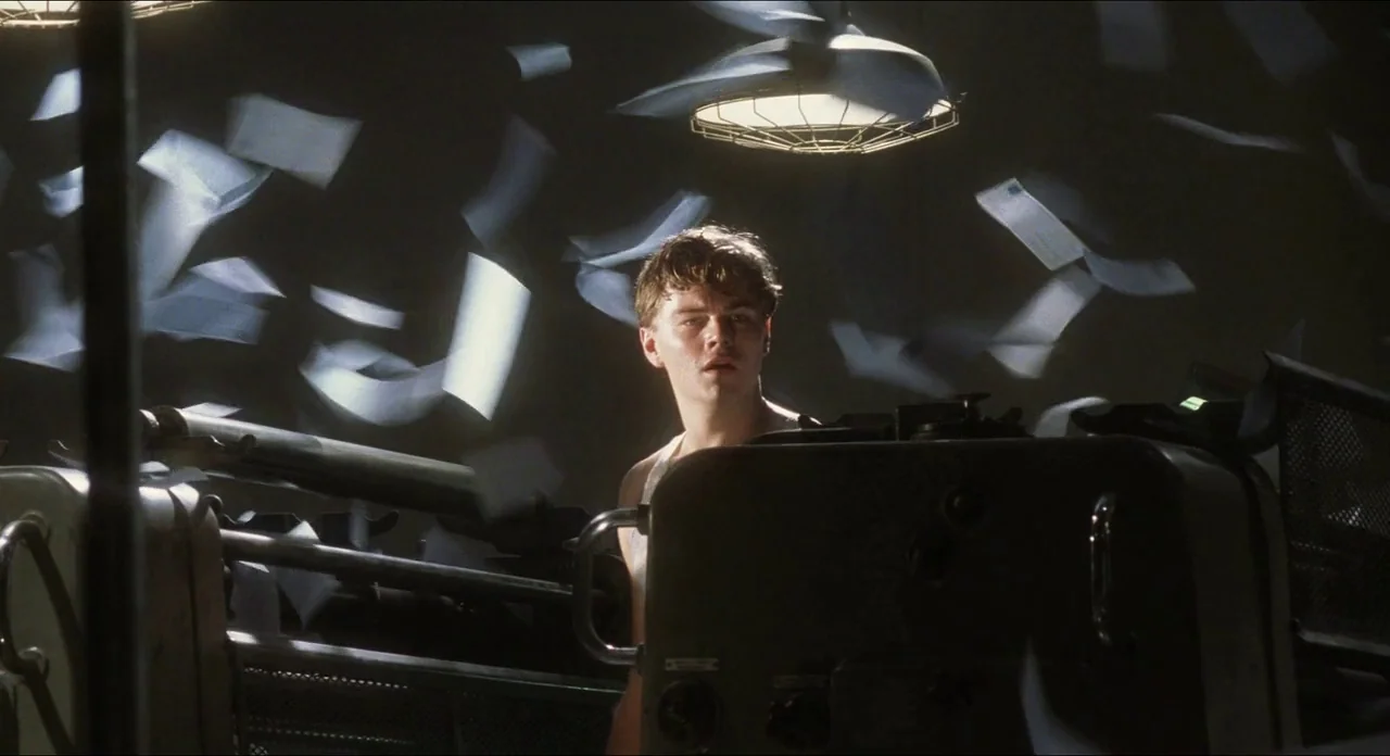 Catch Me If You Can (2002) movie still: medium — A dimly lit industrial print shop contains heavy mechanical printing equipment and swirling paper.…