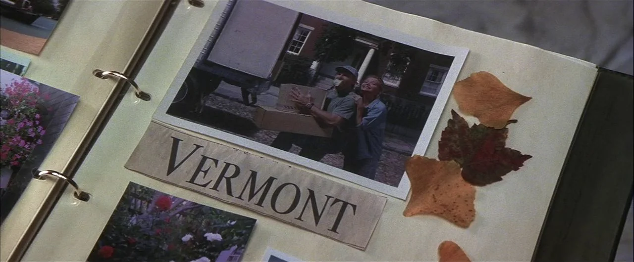 What Lies Beneath (2000) movie still: closeup — A scrapbook page features a photograph of two people carrying boxes with a label. The text 'VERMONT'…