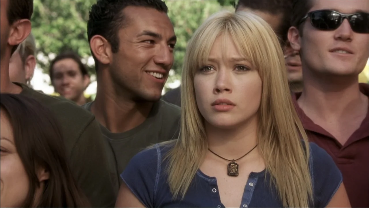 A Cinderella Story (2004) movie still: medium — A group of young adults stands together outdoors during a sunny day. A blonde woman in a blue shirt…