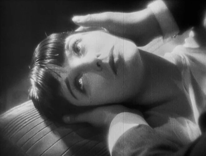 Pandora’s Box (1929) movie still: closeup — A dimly lit room focuses on a woman reclining on a soft surface. A person's hands frame her face from…