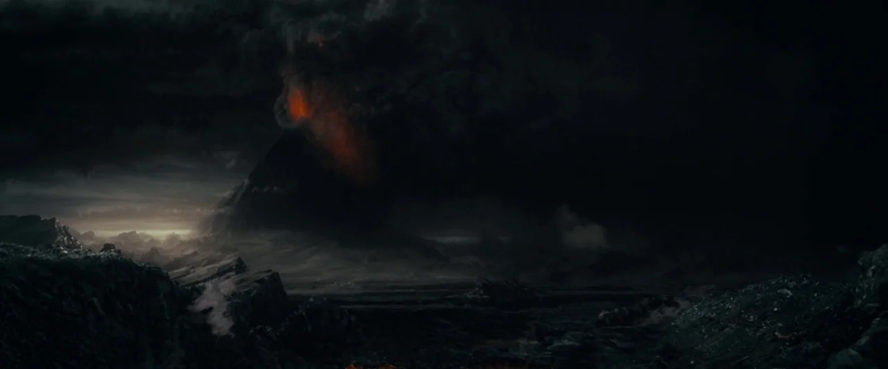 A dark, craggy landscape features a volcanic mountain obscured by heavy, thick smoke clouds. Orange magma glows from within the vent of the active, erupting mountain peak.