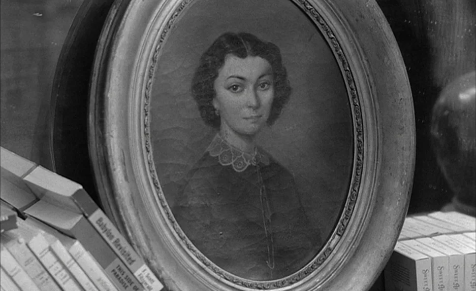 Le Feu Follet (1963) movie still: closeup — A framed oval painting of a woman is centered on a shelf. Stacks of paperbound books frame the portrait…