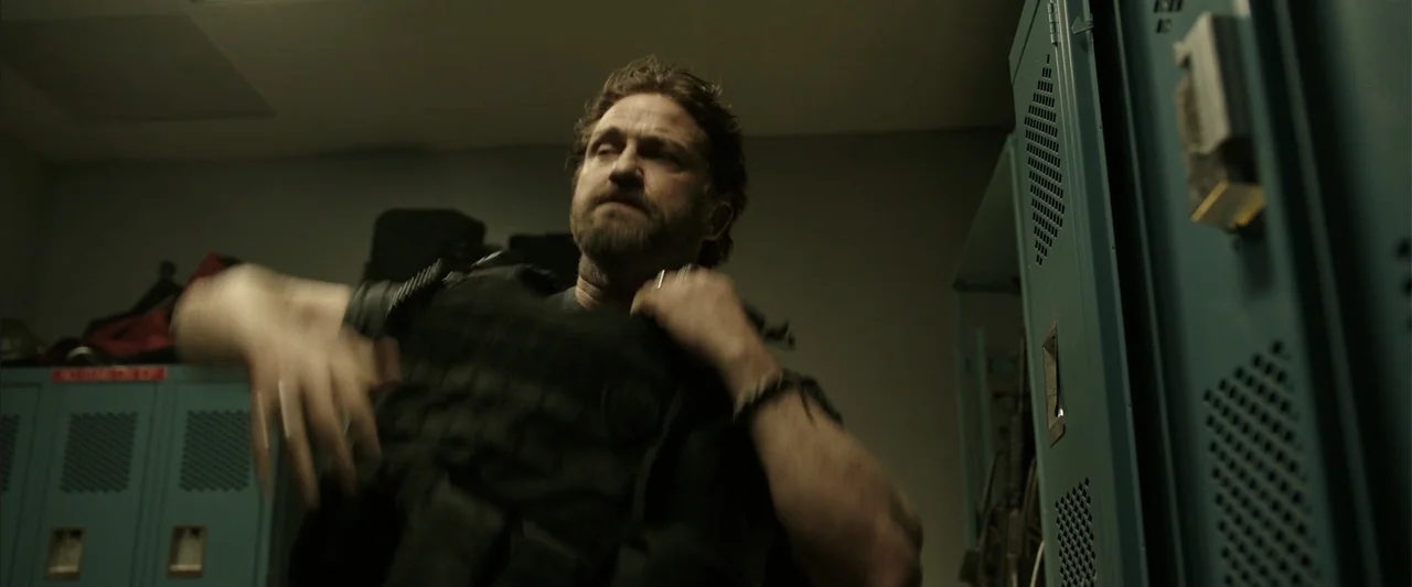 Den of Thieves (2018) movie still: medium — A dimly lit industrial room features rows of light blue metal lockers. A man in tactical gear stands in…