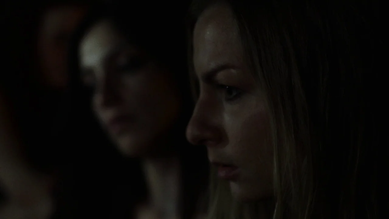 Snowbound (2017) movie still: closeup — A dimly lit interior space is obscured by heavy shadows. Two women are positioned in the frame with one in…