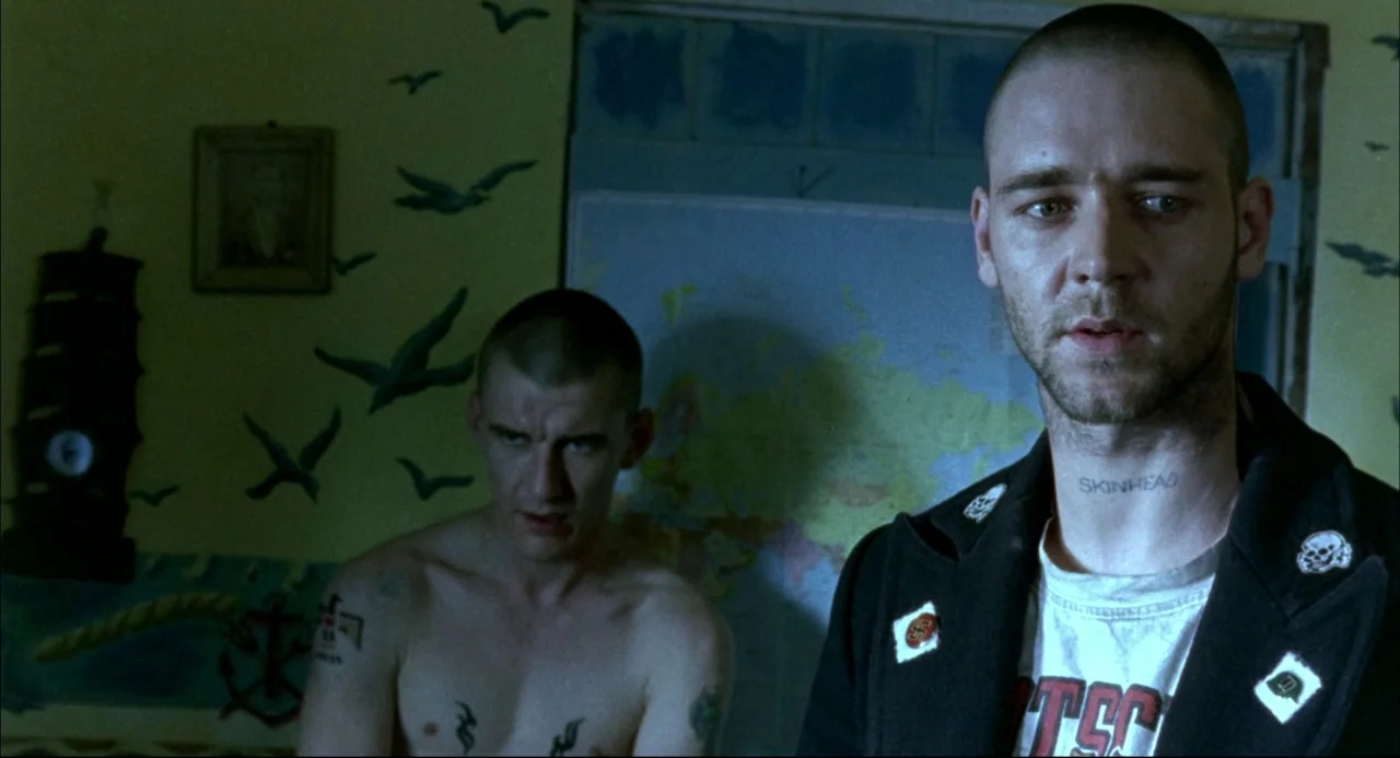 Romper Stomper (1992) movie still: medium — A small room features yellow walls decorated with bird silhouettes and a world map. Two men with shaved…