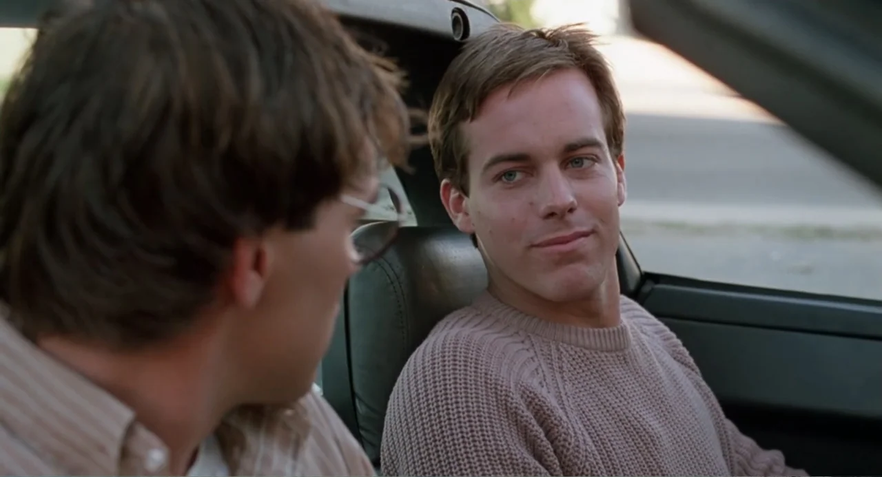 Dangerously Close (1986) movie still: medium — A car interior provides a close setting for two men talking. One man sits in the passenger seat while…