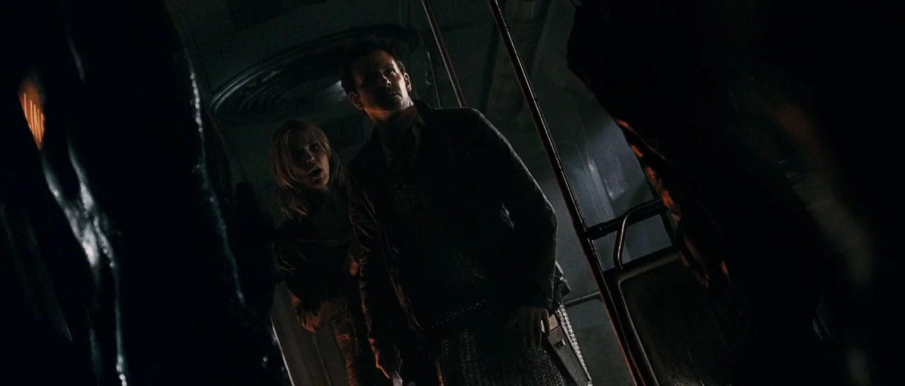 The Midnight Meat Train (2008) movie still: medium — The interior of a dimly lit subway car features metal handrails and dark walls. A man and woman…