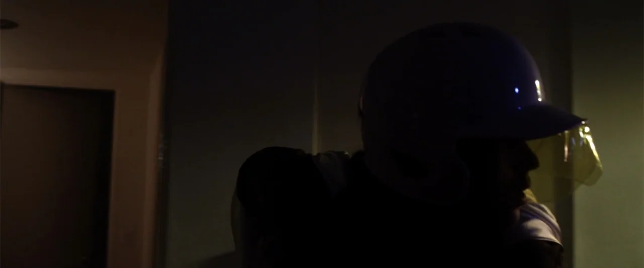 Mermaid Down (2019) movie still: closeup — A dark, dimly lit indoor space features a wall and a doorway in the background. A person wearing a white…
