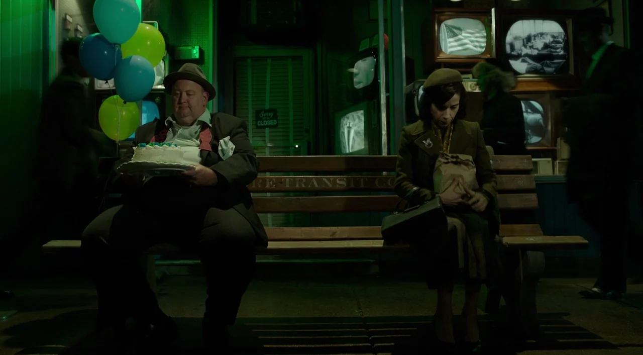 The Shape of Water (2017) movie still: medium — A dark city bus stop at night features a green-lit storefront window with televisions. An older man…