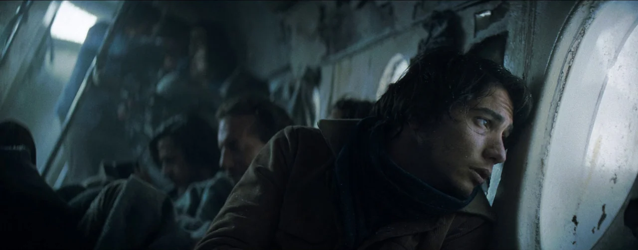 Society of the Snow (2023) movie still: medium — A dimly lit aircraft cabin features rows of passengers seated in cramped, industrial-style chairs.…