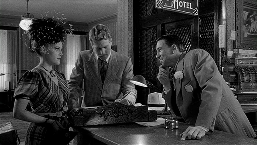 Paper Moon (1971) movie still: medium — A vintage hotel front desk with patterned wallpaper and an old-fashioned cash register. Two travelers engage…