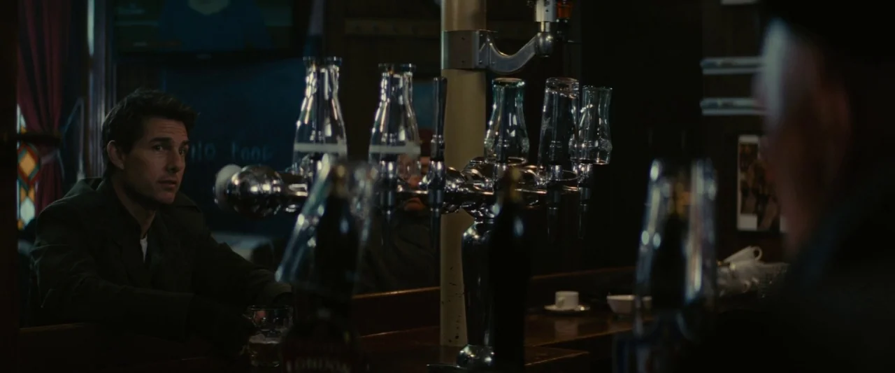Edge of Tomorrow (2014) movie still: medium — A dimly lit pub with a polished wooden bar and a central draught tap system. A man sits at the bar and…