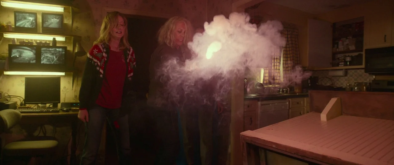 Halloween (2018) (2018) movie still: medium — A dimly lit room filled with stacked surveillance monitors emits a thick, glowing smoke cloud. Two…