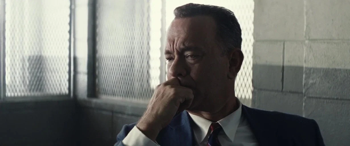 Bridge of Spies (2015) movie still: closeup — An interior space features concrete block walls and a window with chain-link mesh. A middle-aged man…