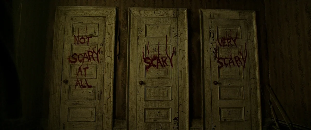 It (2017) movie still: wide — Three weathered white wooden doors are set side by side against dark, peeling wallpaper. Each door features…