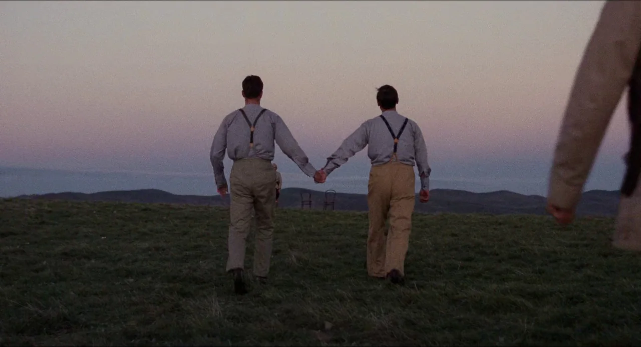 Breaker Morant (1980) movie still: fullbody — A grassy, open hilltop under a clear, pale purple dusk sky. Two men in period-appropriate shirts and…