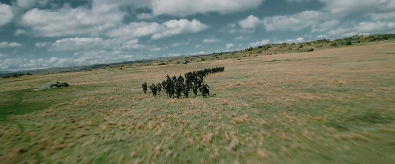 The Lord of The Rings: The Two Towers (2002) movie still: wide — A vast, grassy expanse under a cloudy sky with rolling hills in the distance. A…