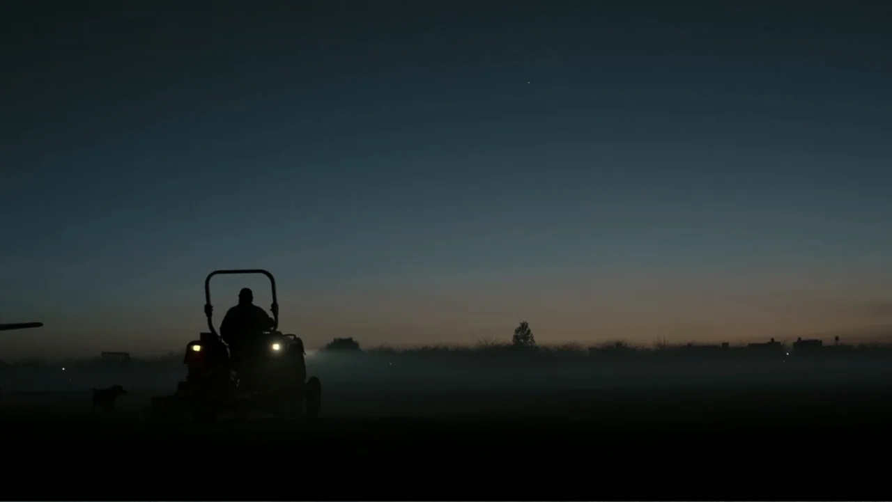 Transfers (2024) movie still: wide — A flat, misty expanse stretches toward a dark horizon under a deep blue morning sky. A lone person operates a…