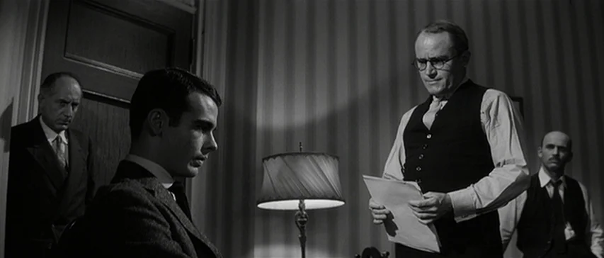Compulsion (1959) movie still: medium — A dimly lit room with striped wallpaper features a small lamp on a table. Four men are gathered in the space…