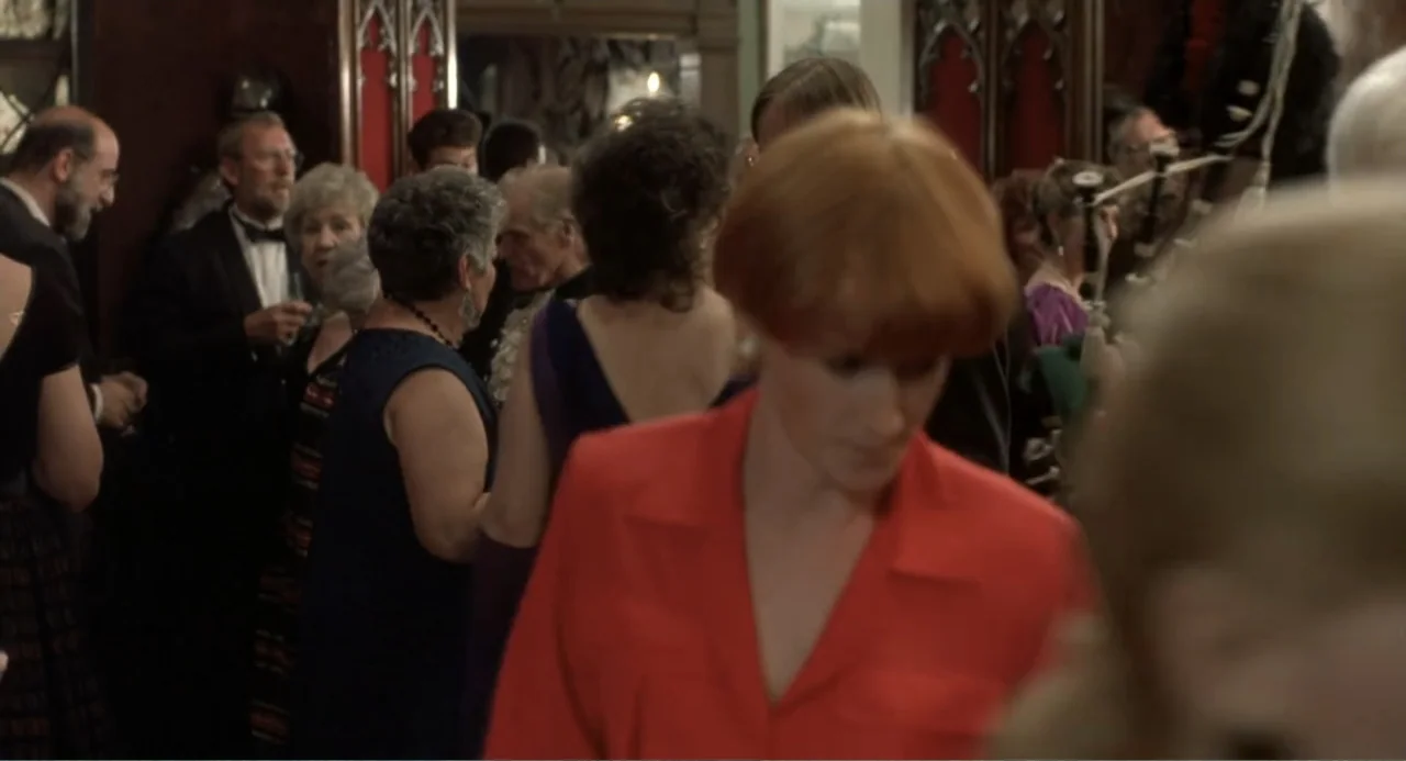 Four Weddings and a Funeral (1994) movie still: medium — A group of people in formal attire gather in a dimly lit, wood-paneled room. A woman with…