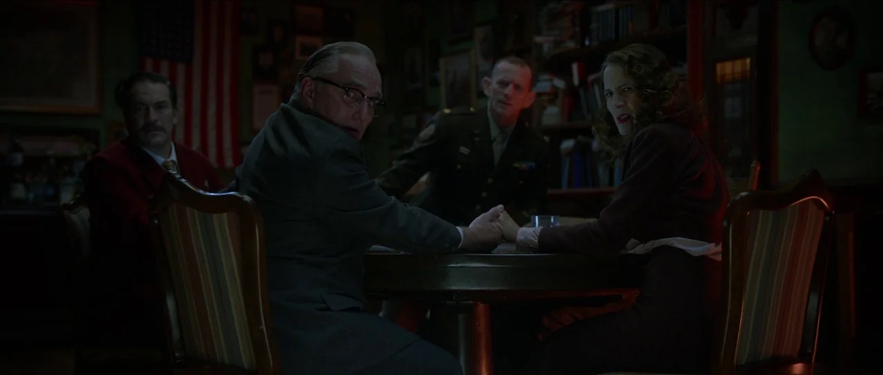 Brooklyn 45 (2023) movie still: medium — A dimly lit tavern environment features dark wood furniture and vintage wall decor. Four individuals sit…