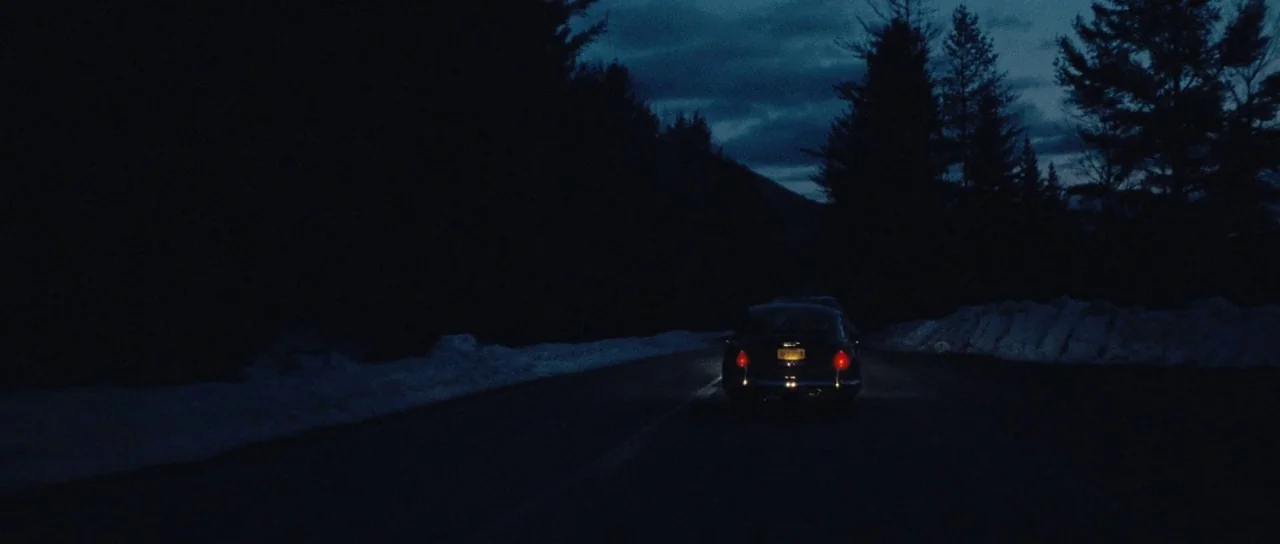 On The Road (2012) movie still: wide — A dark, snow-covered road winds through a dense forest at night under deep blue skies. A single car travels…